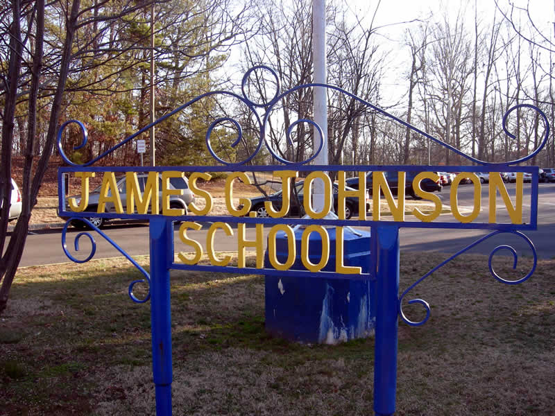 A yellow and blue sign that reads "James G Johnson School" sits outside on a lawn.